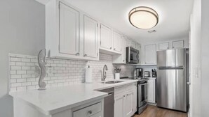 Una cocina moderna con armarios blancos, un refrigerador de acero inoxidable, un microondas y un horno empotrado.