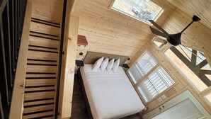 A compact wooden cabin room with a bed, a window, a ceiling fan, and a radiator. - Cozy 2-bedroom cabin # 101 (Moab)