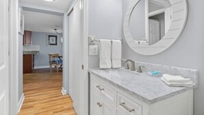 Un baño con un espejo redondo, tocador blanco y piso de madera.