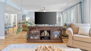 Una sala de estar moderna con un televisor de pantalla plana, un mueble de entretenimiento de madera, un sofá color beige y un comedor al fondo.