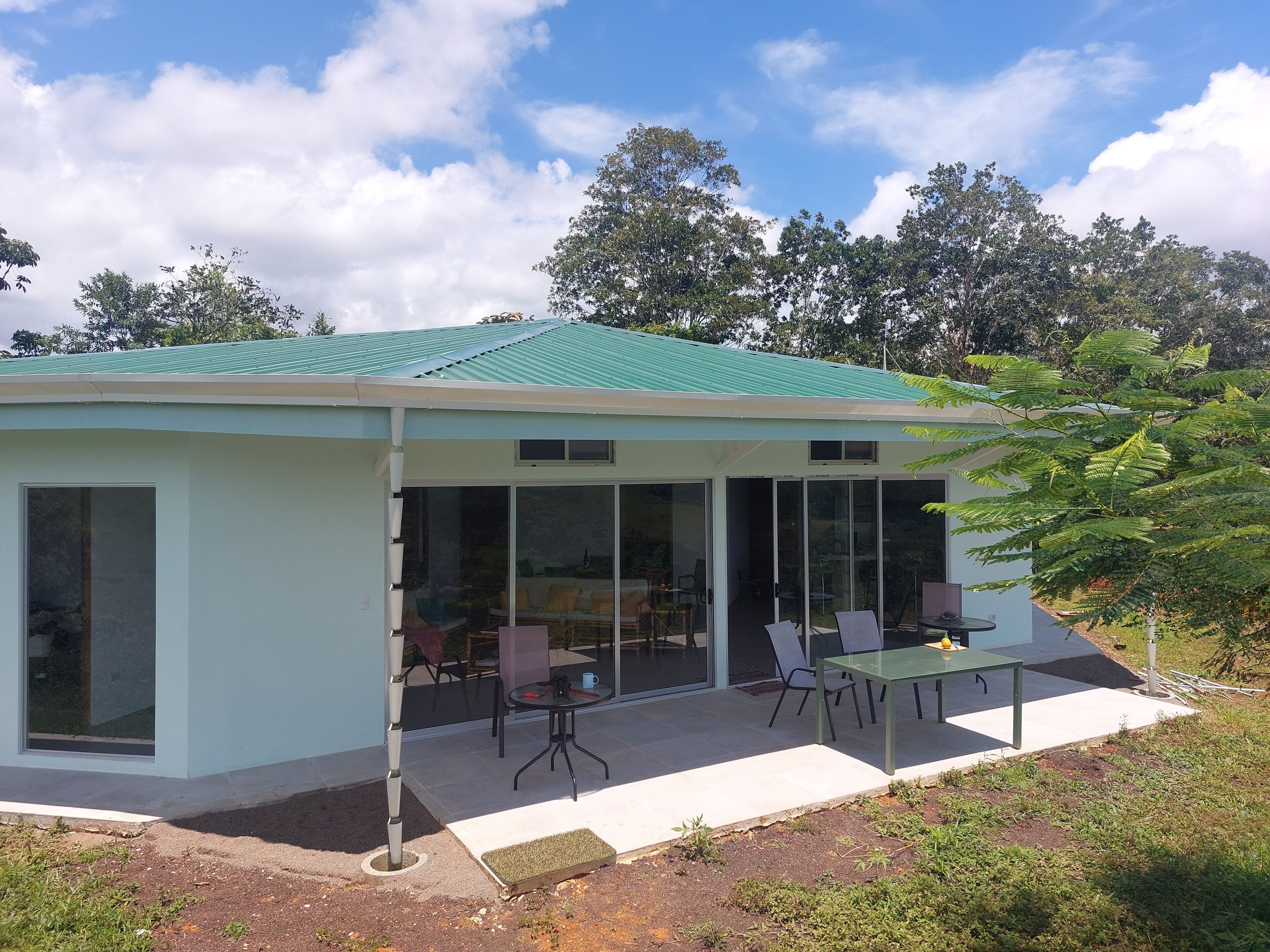 A modern house with a green roof, large glass doors, and a patio with outdoor furniture.