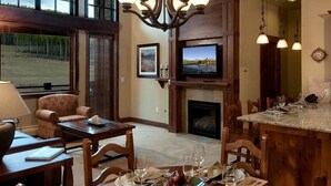 A cozy living room with a fireplace, a television, and a dining area set for a meal. - Exquisite ski-in, ski-out! 1 or 2-bedroom condo on Peak 7 in Breckenridge! (Breckenridge)