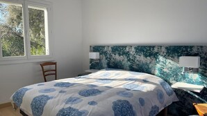 A bedroom with a bed, a chair, a bedside table, a lamp, and a window.