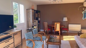 A living room with a TV, wooden furniture, patterned chairs, a dining table, and a sofa.