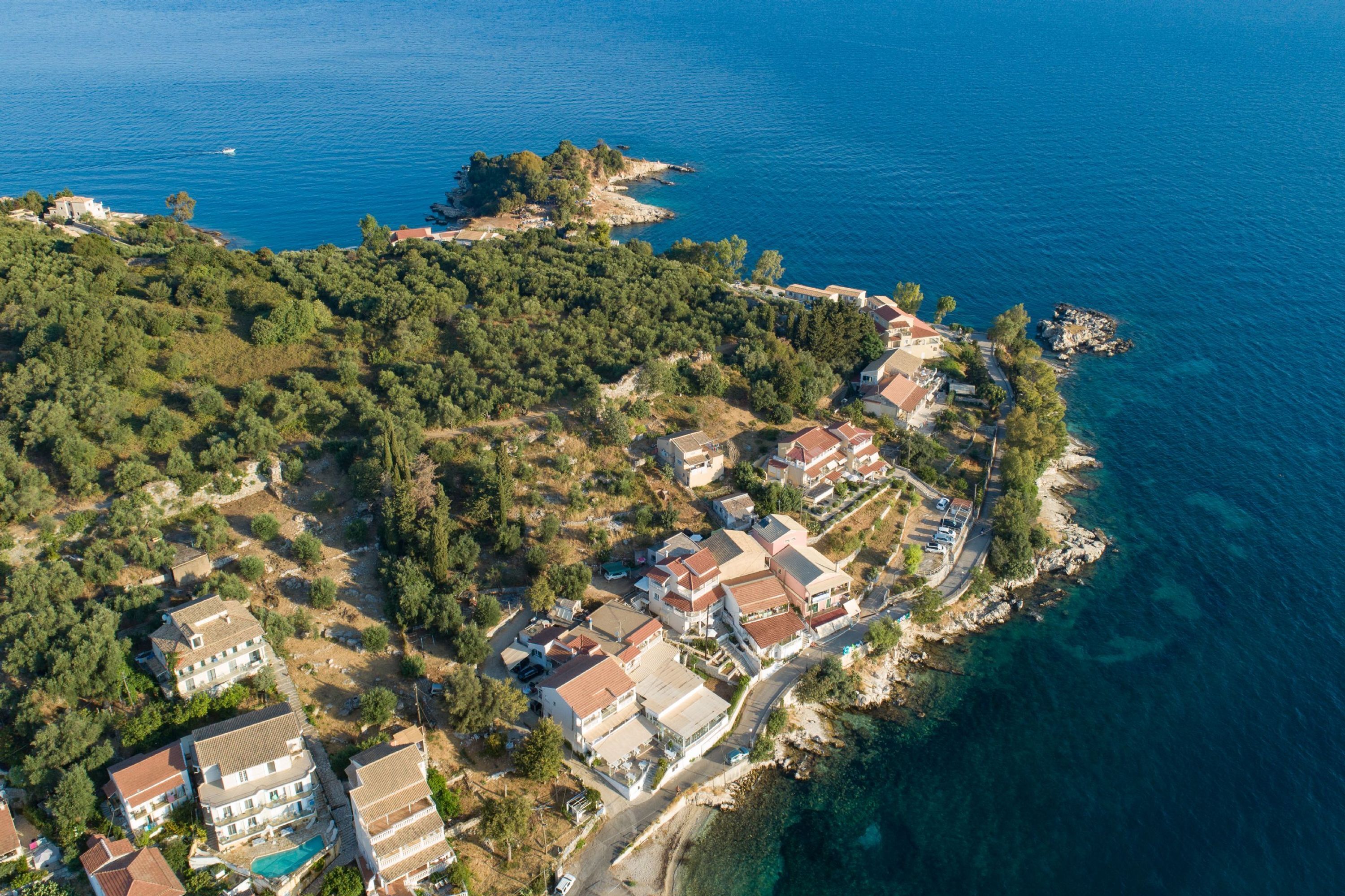 An aerial view of a coastal residential area with houses, a road, and a clear blue sea.