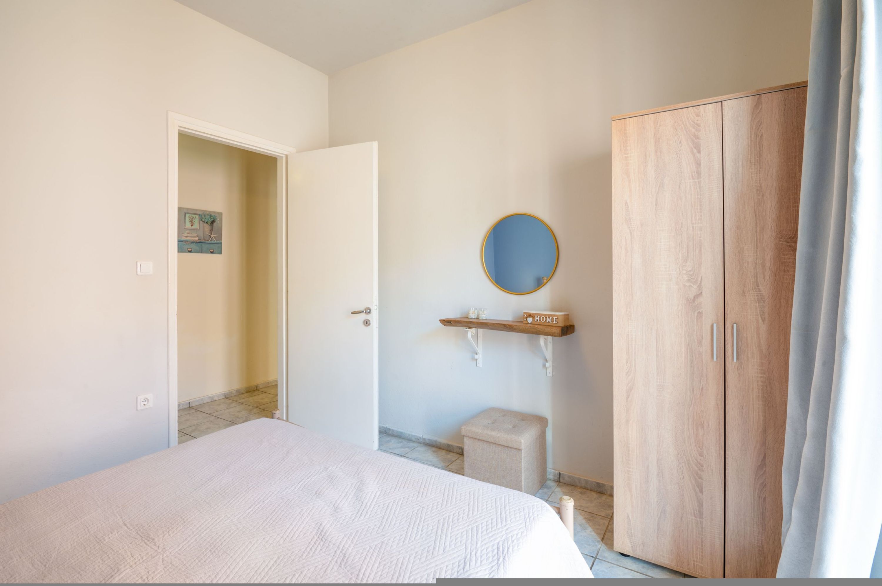 Ein Schlafzimmer mit einem Bett, einem Holzschrank, einem runden Spiegel, einem kleinen Hocker und einem Regal mit einem 'HOME'-Schild.