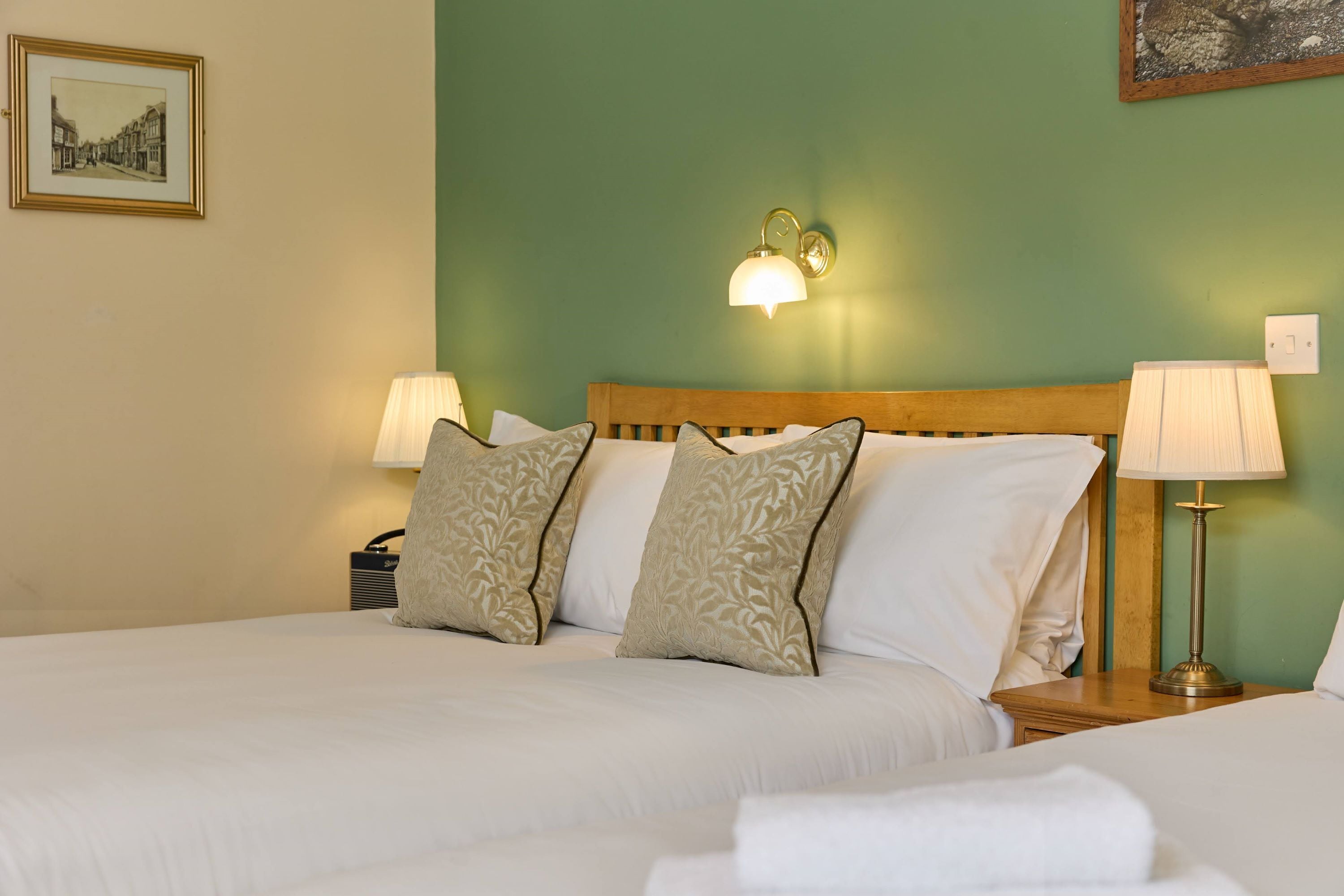 A double bed with two pillows, a nightstand with a lamp, and a wall-mounted light fixture.