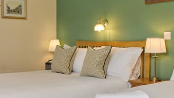 A double bed with two pillows, a nightstand with a lamp, and a wall-mounted light fixture.