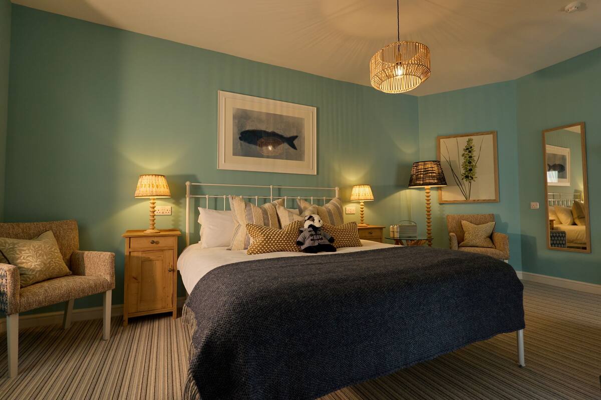A bedroom with a bed, two nightstands, a chair, a hanging light fixture, and a framed picture on the wall.