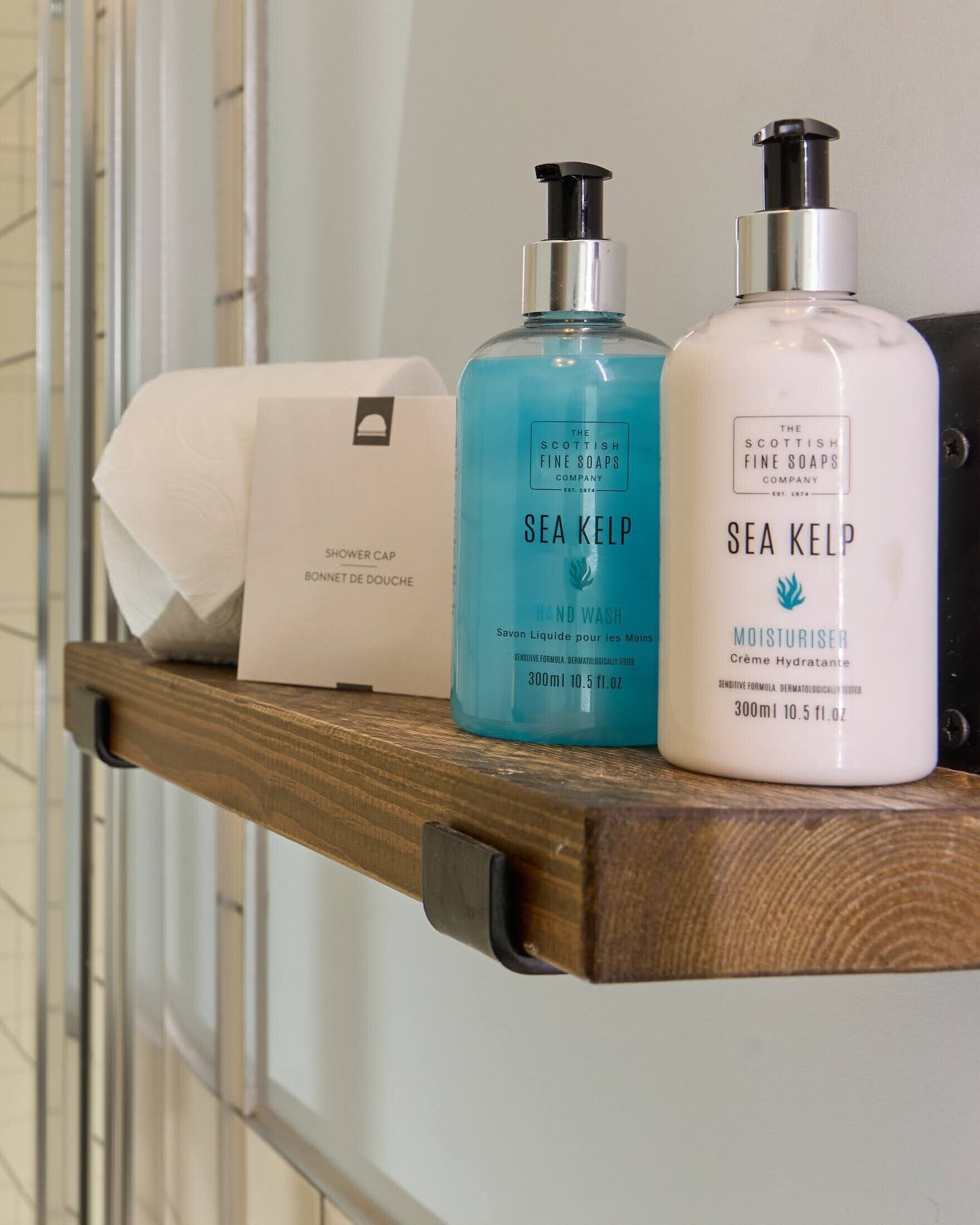 A wooden shelf with two bottles of Sea Kelp hand wash and a shower cap.