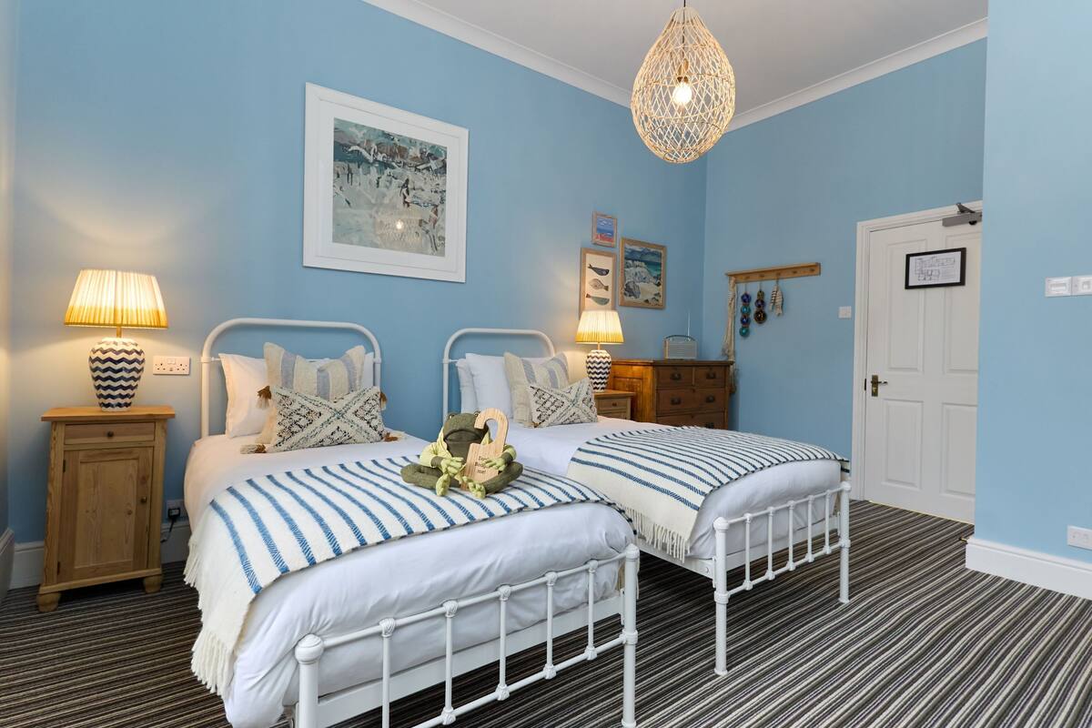A bedroom with two beds, a wooden cabinet, a hanging light fixture, and a framed picture on the wall.