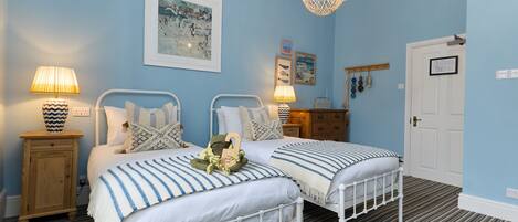 A bedroom with two beds, a wooden cabinet, a hanging light fixture, and a framed picture on the wall.