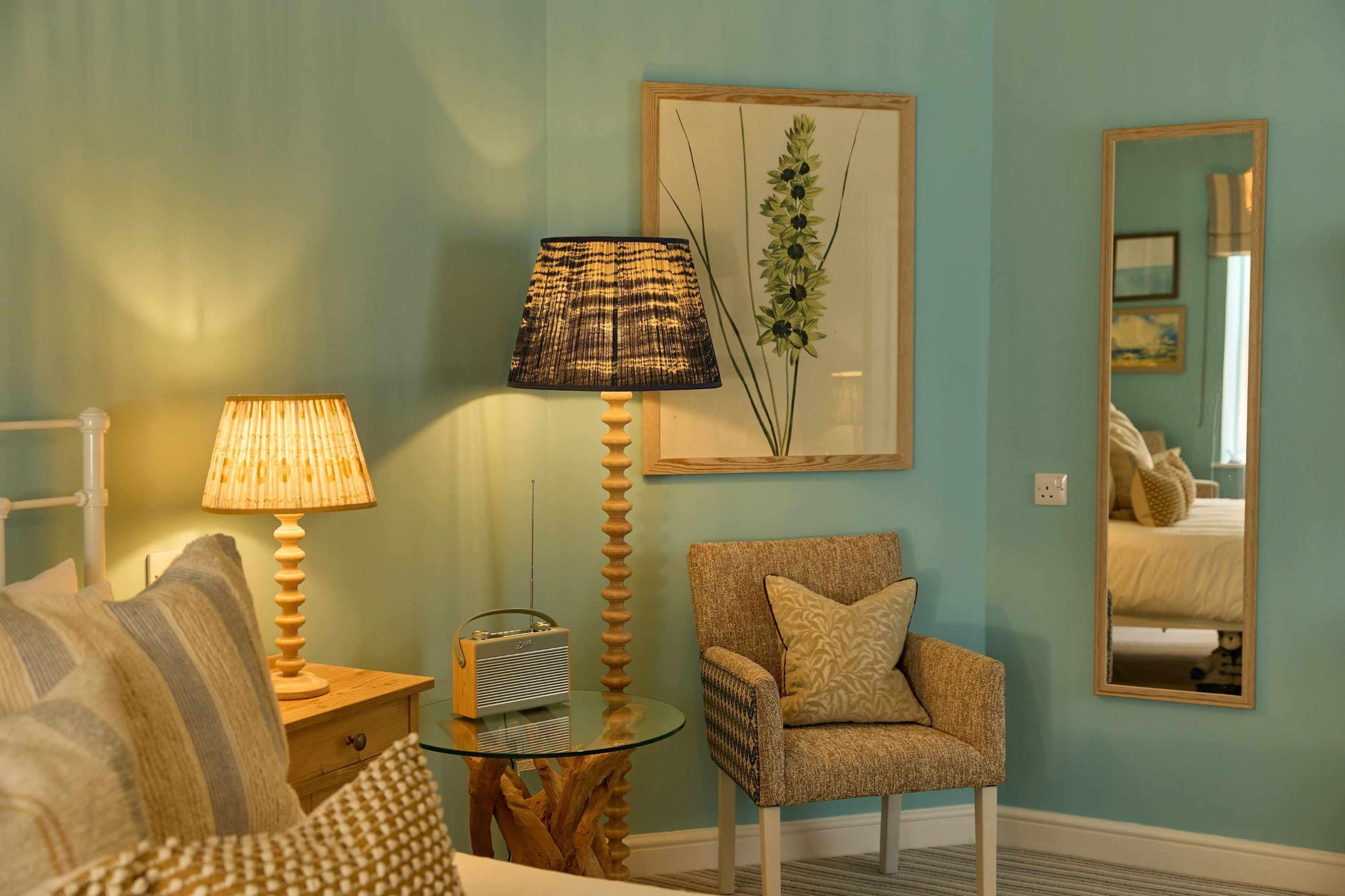 A room with a sofa, a chair, a lamp, a radio, and a framed plant.