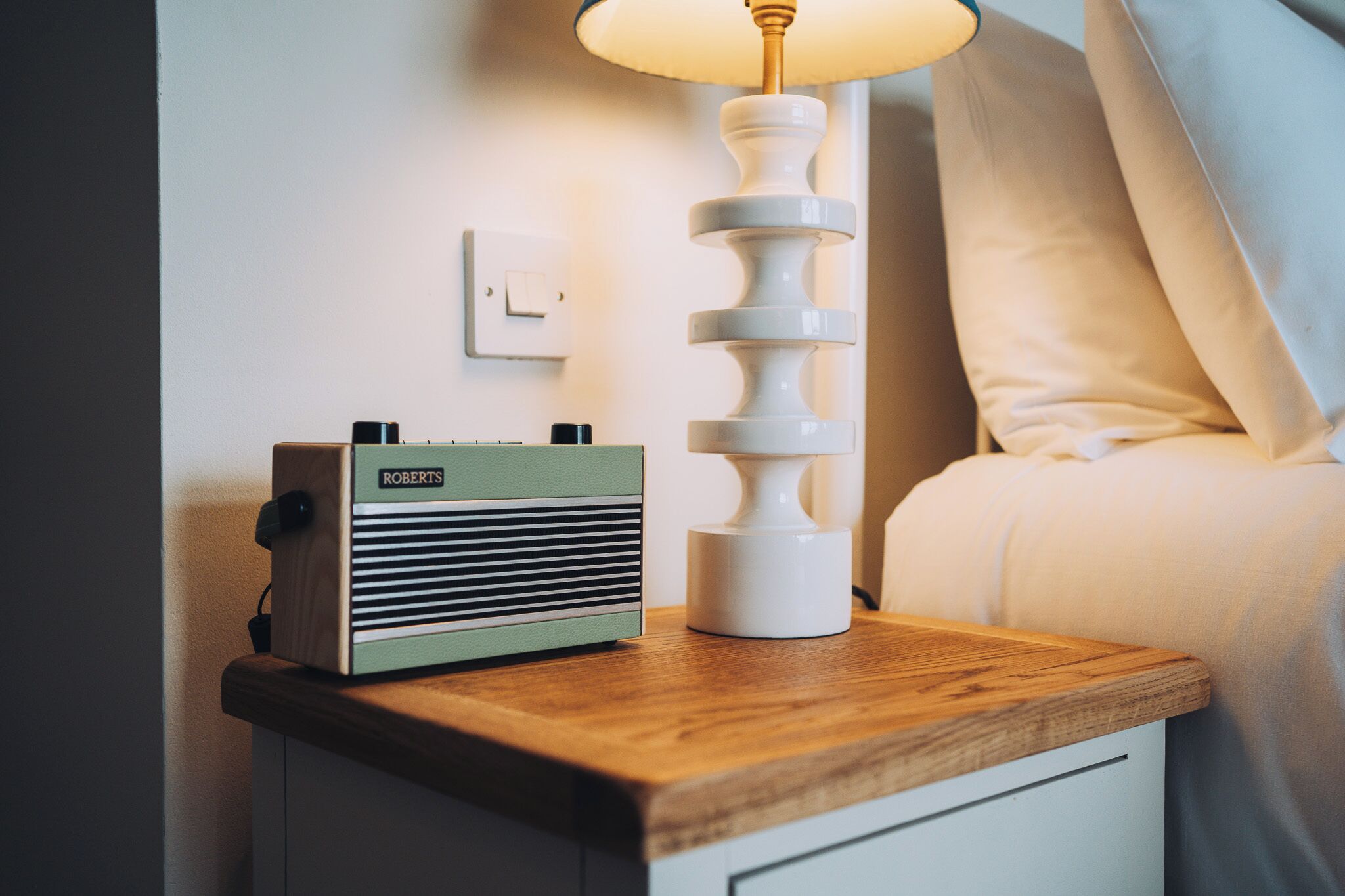 A wooden bedside table with a vintage radio and a modern lamp.