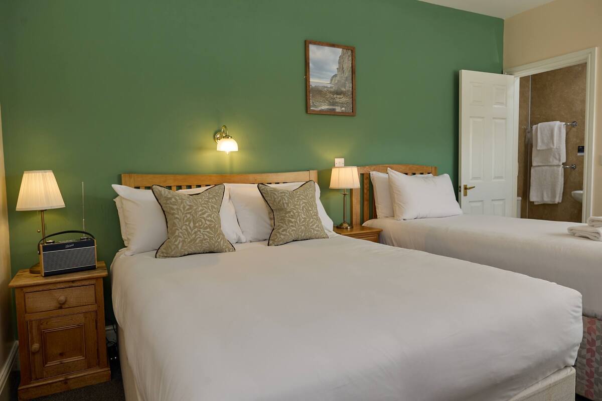 A hotel room with two beds, a nightstand with a radio, and a door leading to a bathroom.