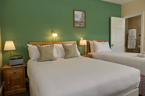 A hotel room with two beds, a nightstand with a radio, and a door leading to a bathroom. - The Dolphin (Beer)
