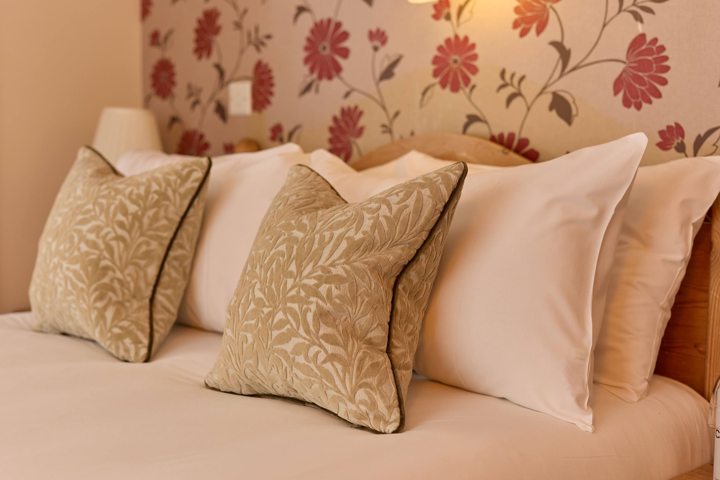 Un canapé avec des coussins beige et blancs, un papier peint à motifs floraux et une tête de lit en bois.