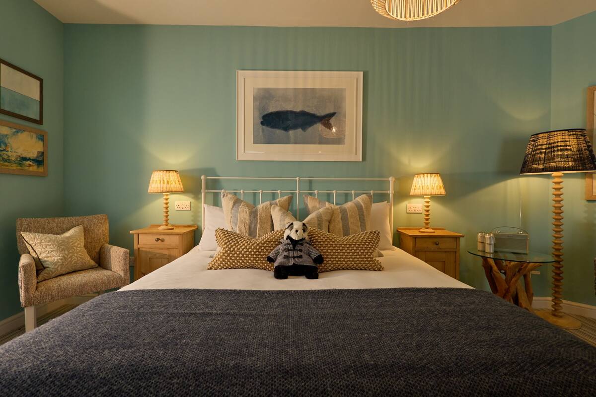 A neatly arranged bedroom with a bed, pillows, a chair, and a bedside table with lamps.