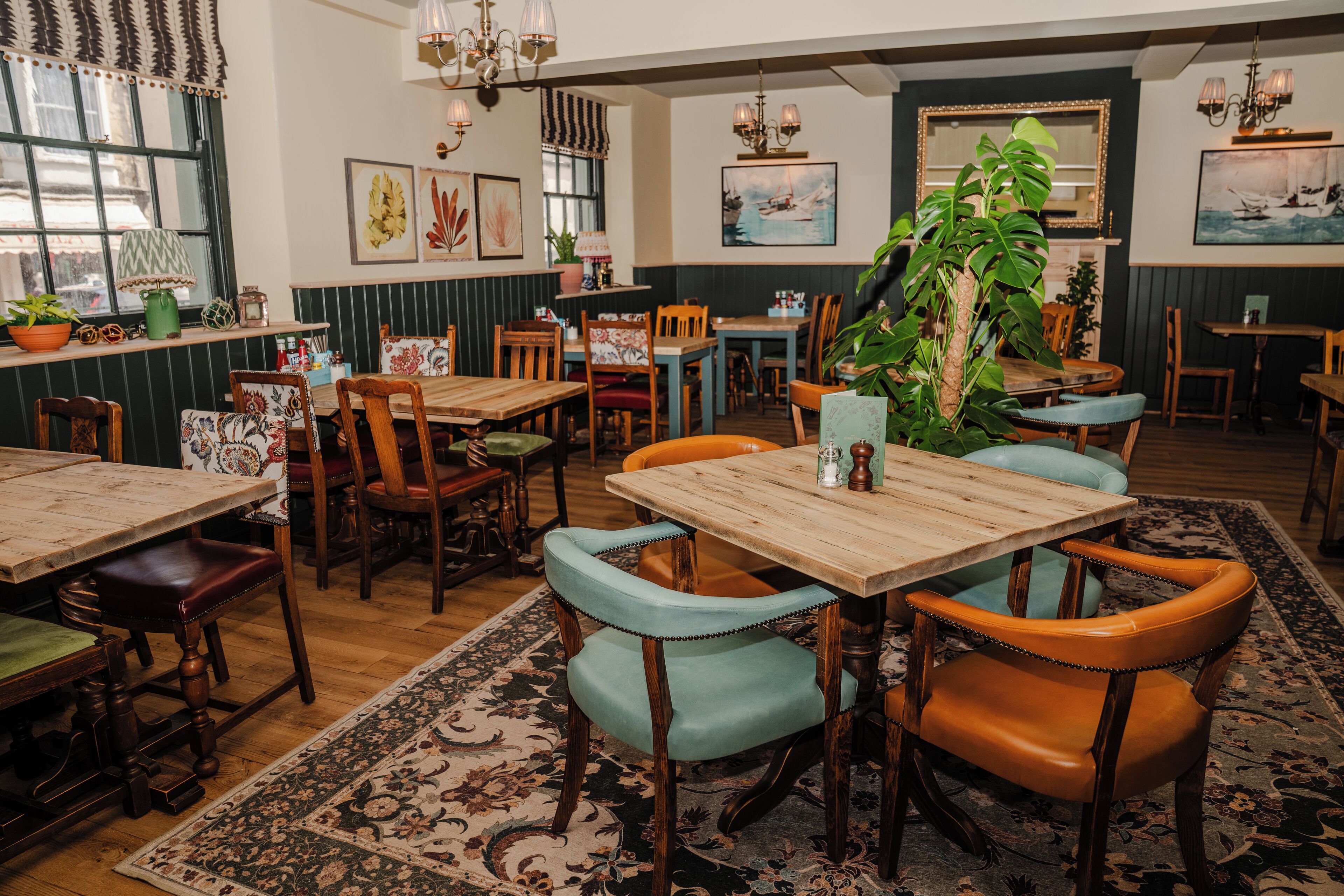 A cozy restaurant interior with wooden tables and chairs, potted plants, and artwork on the walls.