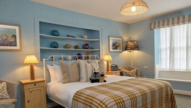 A neatly arranged bedroom with a bed, bedside tables, a shelf with decorative items, and a window with curtains. - The Dolphin (Beer)