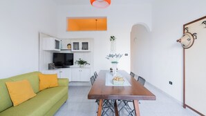 Een moderne woonkamer met een groene bank, een houten eettafel en een keuken met witte kasten en een televisie.