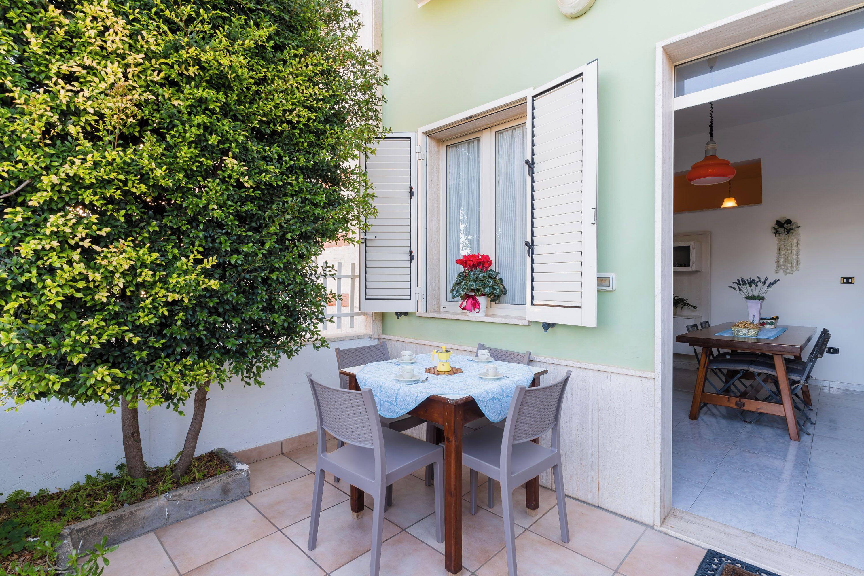 A dining area with a table set for four, surrounded by chairs, and a window with white shutters.