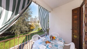 Un balcon avec une table dressée pour deux personnes, des chaises, un auvent à rayures et une vue sur le jardin.