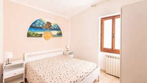 Une chambre à coucher comprenant un lit, des tables de chevet, une commode, une fenêtre et une œuvre d’art accrochée au mur.