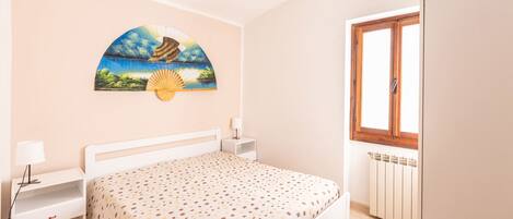 A bedroom with a bed, bedside tables, a nightstand, a window, and a wall-mounted artwork.
