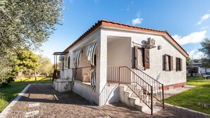 Une petite maison de plain-pied, avec un toit recouvert de tuiles rouges, une véranda et un escalier menant à l’entrée.