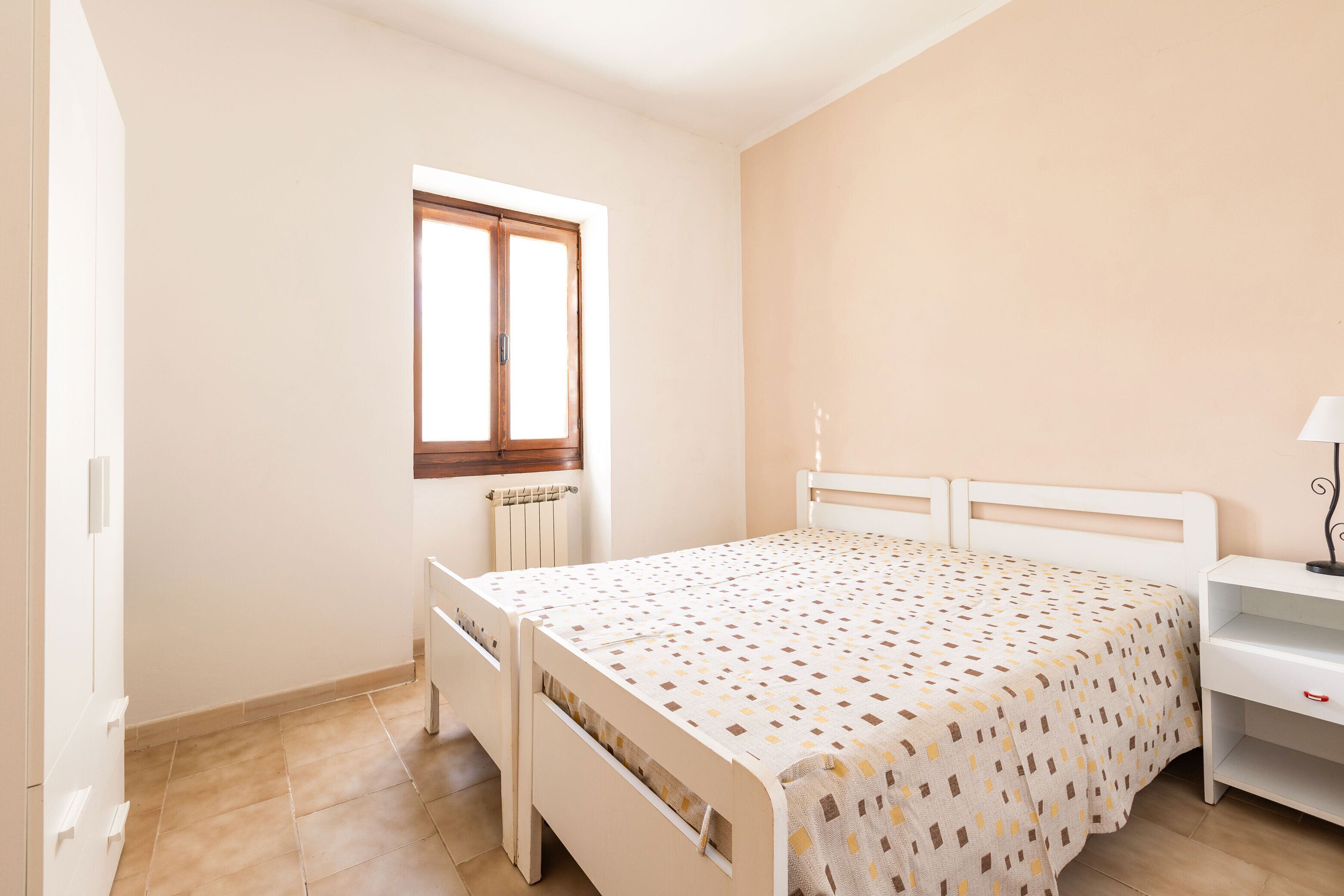 Een slaapkamer met een bed, nachtkastje, raam en radiator.