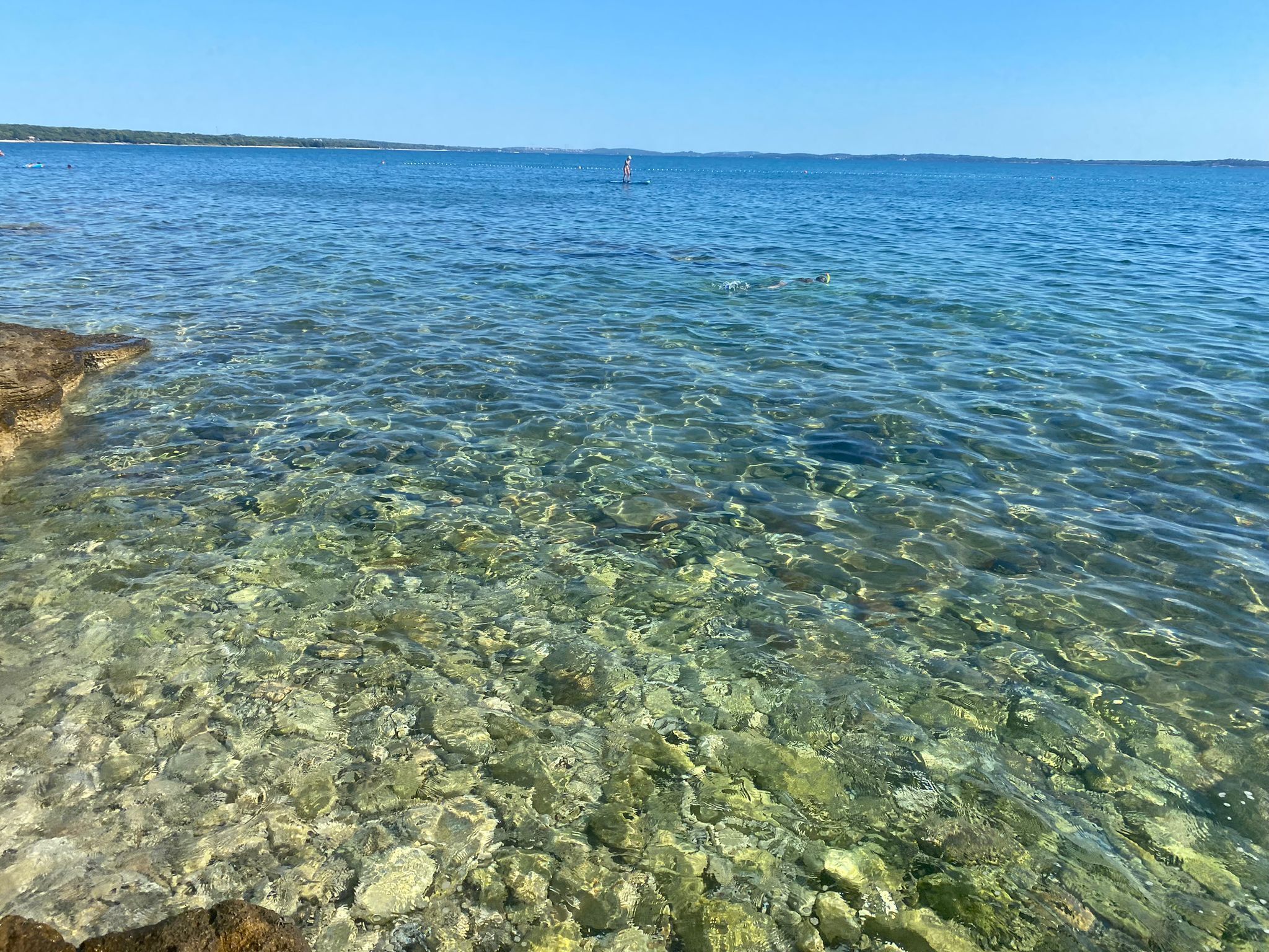 A clear view of a rocky shoreline with calm water extending to the horizon.