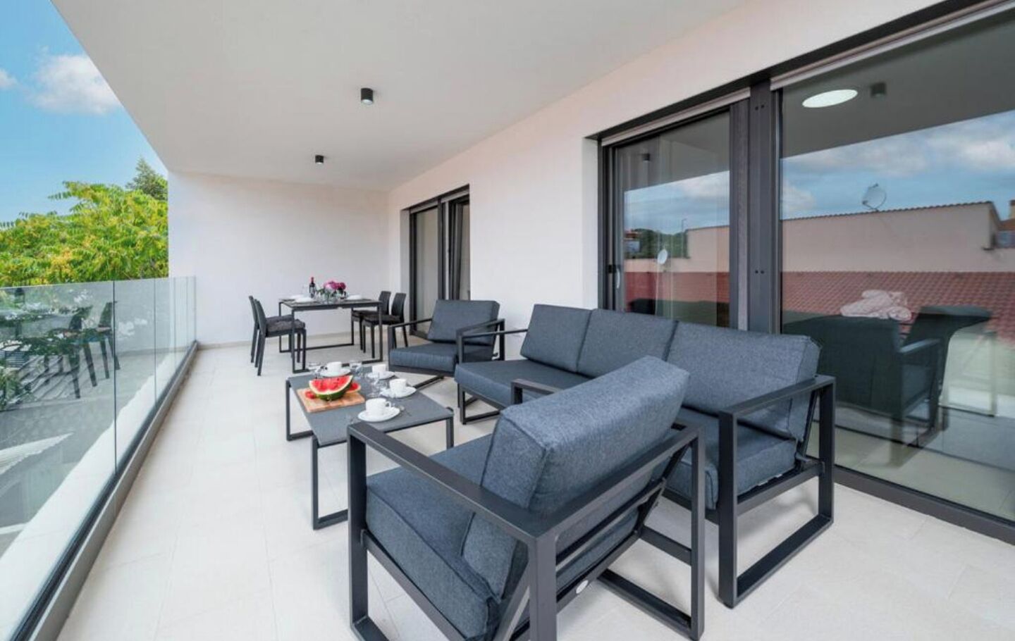 En balkon med siddeplads, inklusive sofaer og et bord med vandmelon og kopper.