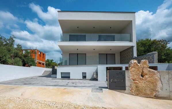 Una casa moderna de dos pisos con techo plano, ventanas amplias y una escultura de piedra al frente.