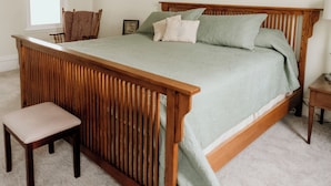 Ein Schlafzimmer mit einem hölzernen Bett, einer Holzbank, einem Nachttisch und einer Pendelleuchte.
