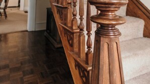 Eine hölzerne Treppe mit Handlauf und Spindeln, die zu einer Plattform mit weißem Teppich führt.