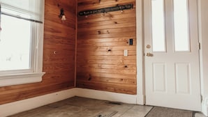 Ein Zimmer mit Holzwänden, einer weißen Tür und einem Fenster mit Jalousien.