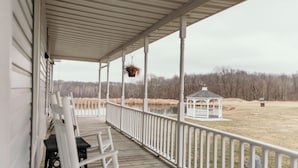 Eine überdachte Veranda mit weißen Schaukelstühlen und einem weißen Gazebo im Hintergrund.