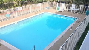A rectangular swimming pool with a white fence, surrounded by trees and a few lounge chairs. - AMERICAN INN (Temple)