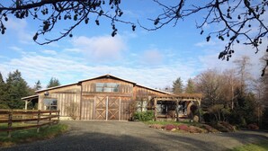 A rustic barn with a large garage door, surrounded by a gravel driveway and a wooden fence. - 40 Acre Estate, Beach Access, Horses, Sleeps up to 6 on Vashon Island (Vashon)