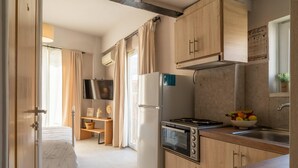 Une cuisine compacte équipée d’un réfrigérateur, d’une cuisinière et d’un petit évier. On y trouve également une télévision et une fenêtre avec des rideaux.