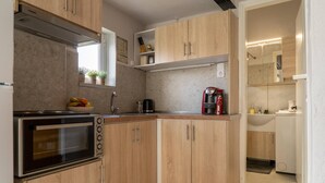 Une cuisine compacte avec des meubles en bois, un four encastré, une machine à café et une fenêtre agrémentée de plantes.