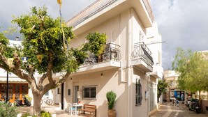 Un immeuble de deux étages avec un balcon, un arbre dans la cour et un scooter garé à l’extérieur.
