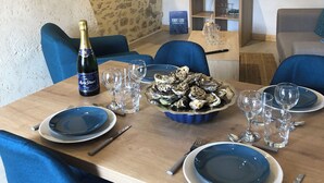 Une table dressée pour le dîner, avec des assiettes bleues, une bouteille de champagne et un plat d’huîtres.