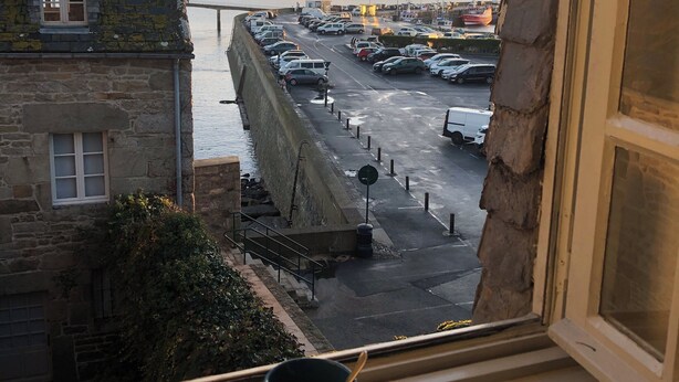 Une vue depuis une fenêtre donnant sur un parking, avec un mur en pierre et un bâtiment doté d’une fenêtre.
