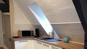 Une cuisine compacte avec des meubles blancs, un four à micro-ondes, une machine à café et un évier.