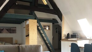 Un espace de vie de style loft comprenant un escalier en bois, un canapé, une table basse et un coin cuisine équipé d’un four à micro-ondes.