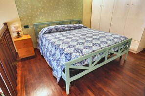 Una cama individual con una colcha de estampado geométrico en una habitación con piso de madera y pared verde.