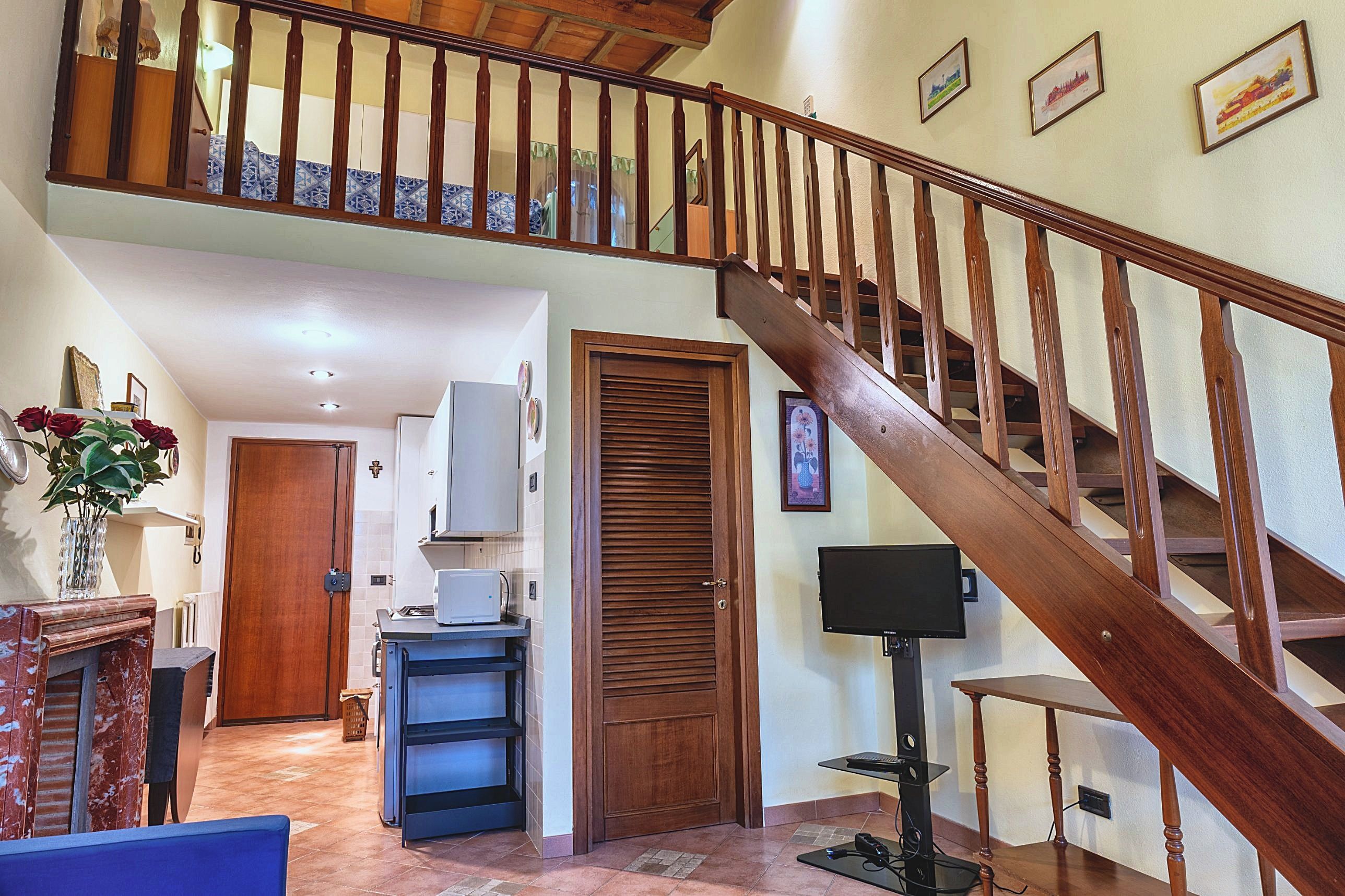 A staircase with wooden balusters leading to an upper floor, a kitchen area with a microwave and a refrigerator, and a dining area with a table and chairs.