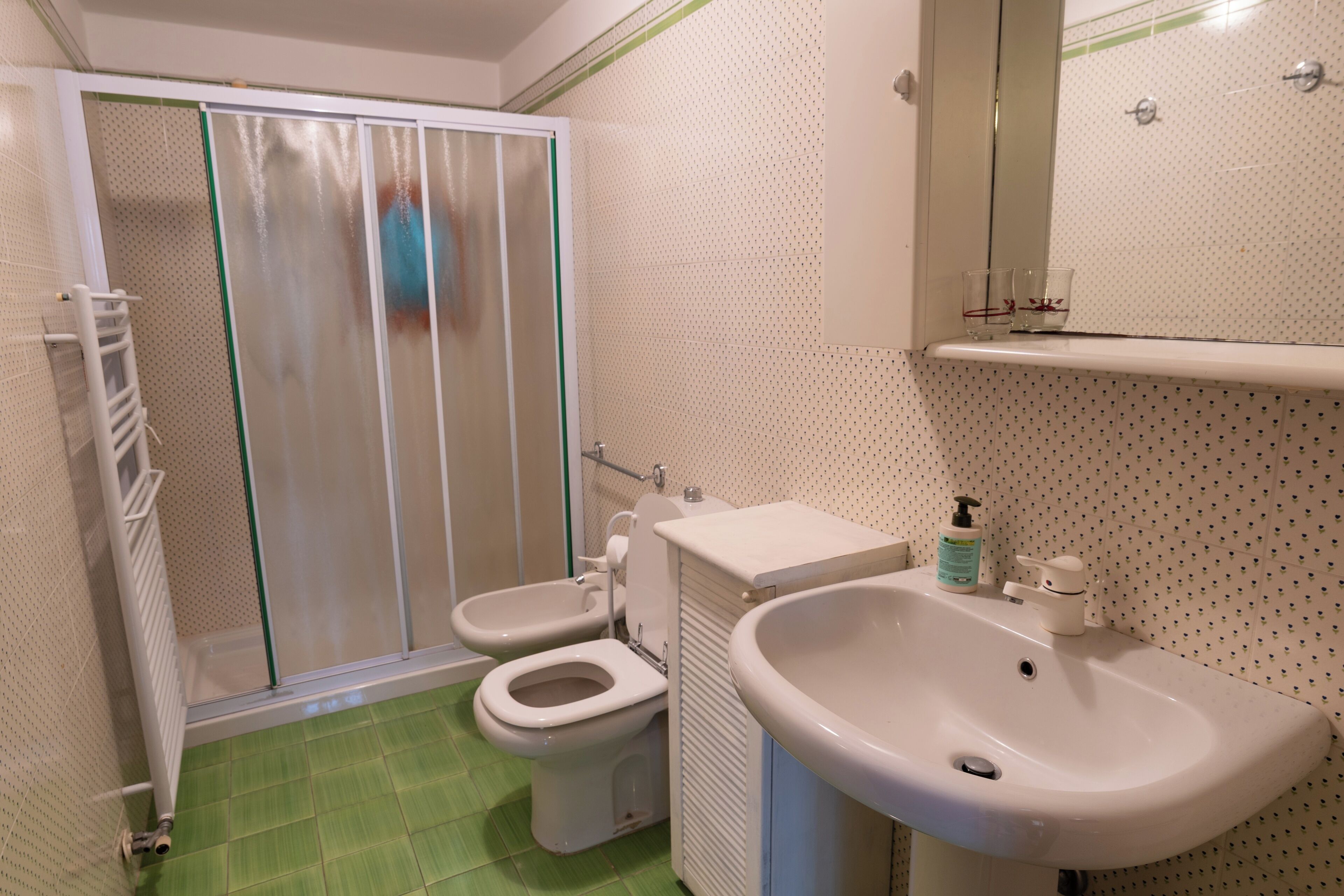 A bathroom with a shower enclosure, two toilets, a sink, and a mirror.
